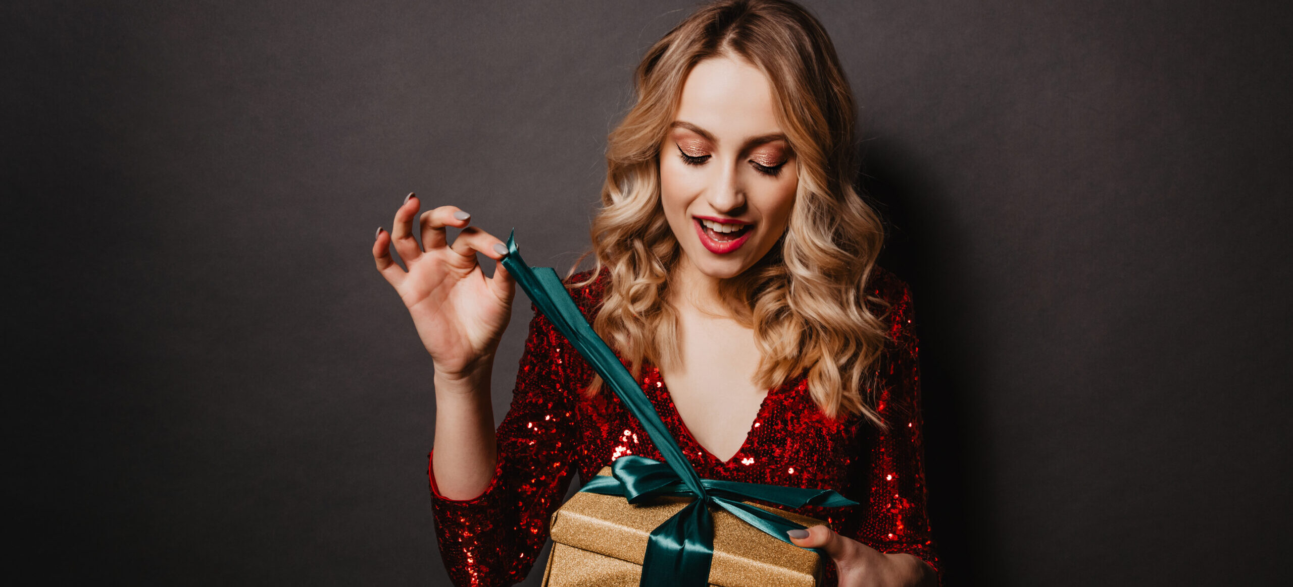 Glad young woman opening her birthday gift. Studio portrait of beautiful blonde teen girl with new year present.