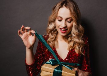 Glad young woman opening her birthday gift. Studio portrait of beautiful blonde teen girl with new year present.